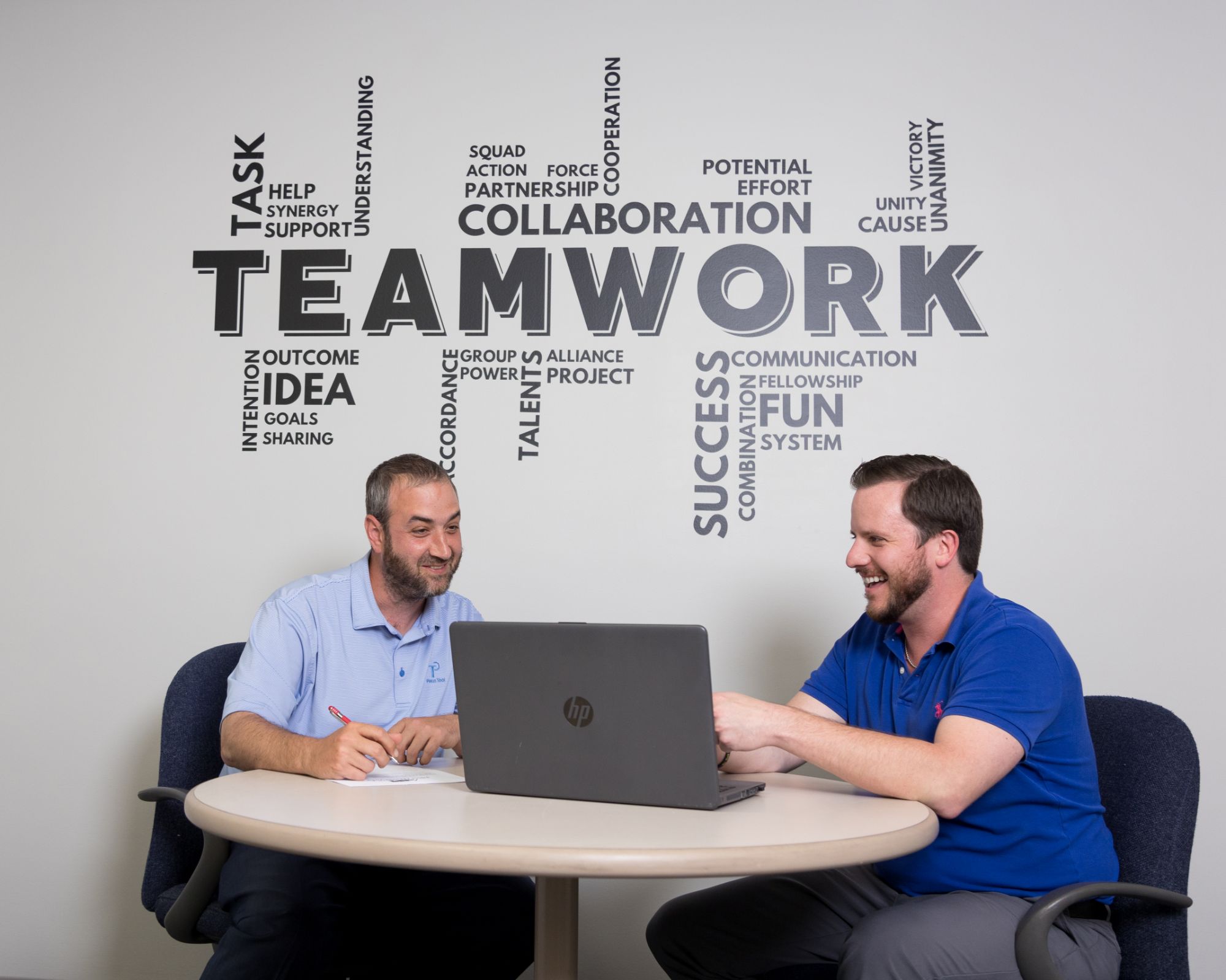 Collegues conversing infront of a wall that has a teamwork decal painted on it