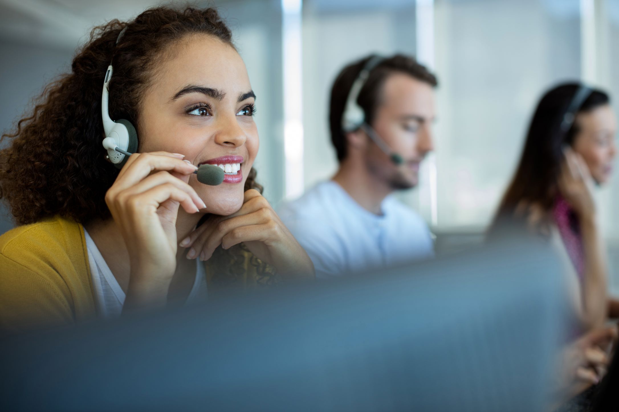 A customer service representative on a headset with two other customer service representatives in the background
