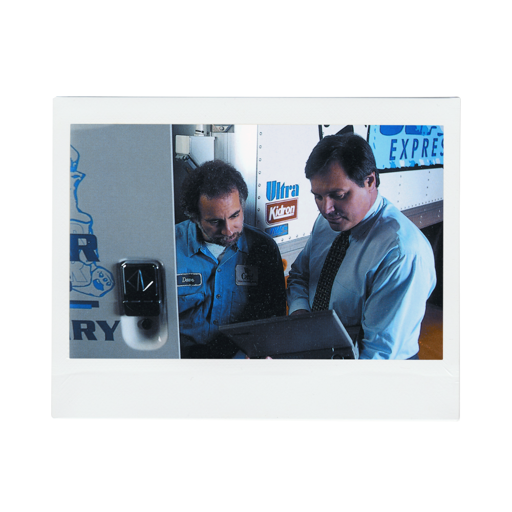 Historical photo of Dave Ghioldi and Ken Singleton looking at a laptop in front of a truck.