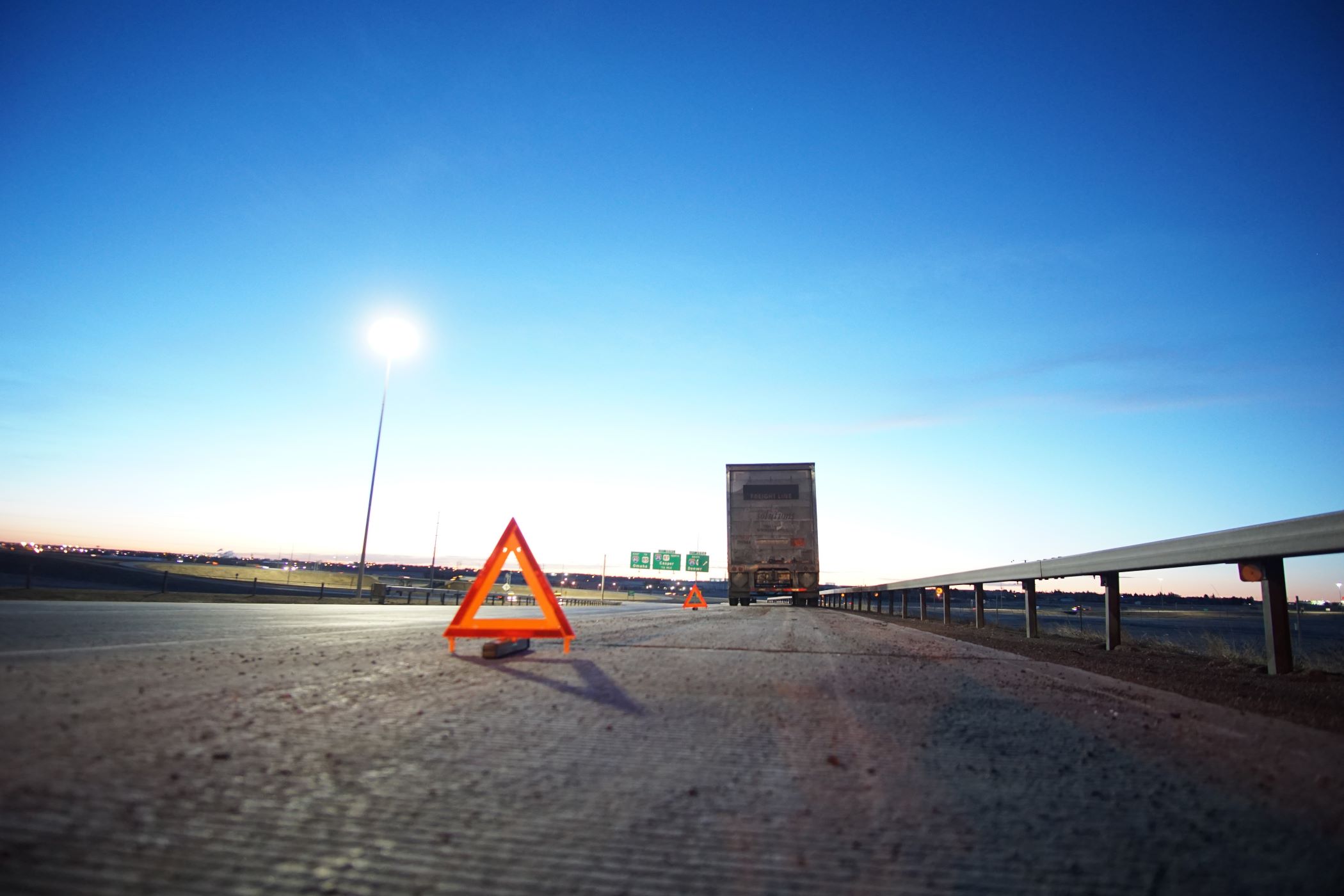 A truck broken down on the side of the highway. Triangular safety signs are placed leading up to the truck.